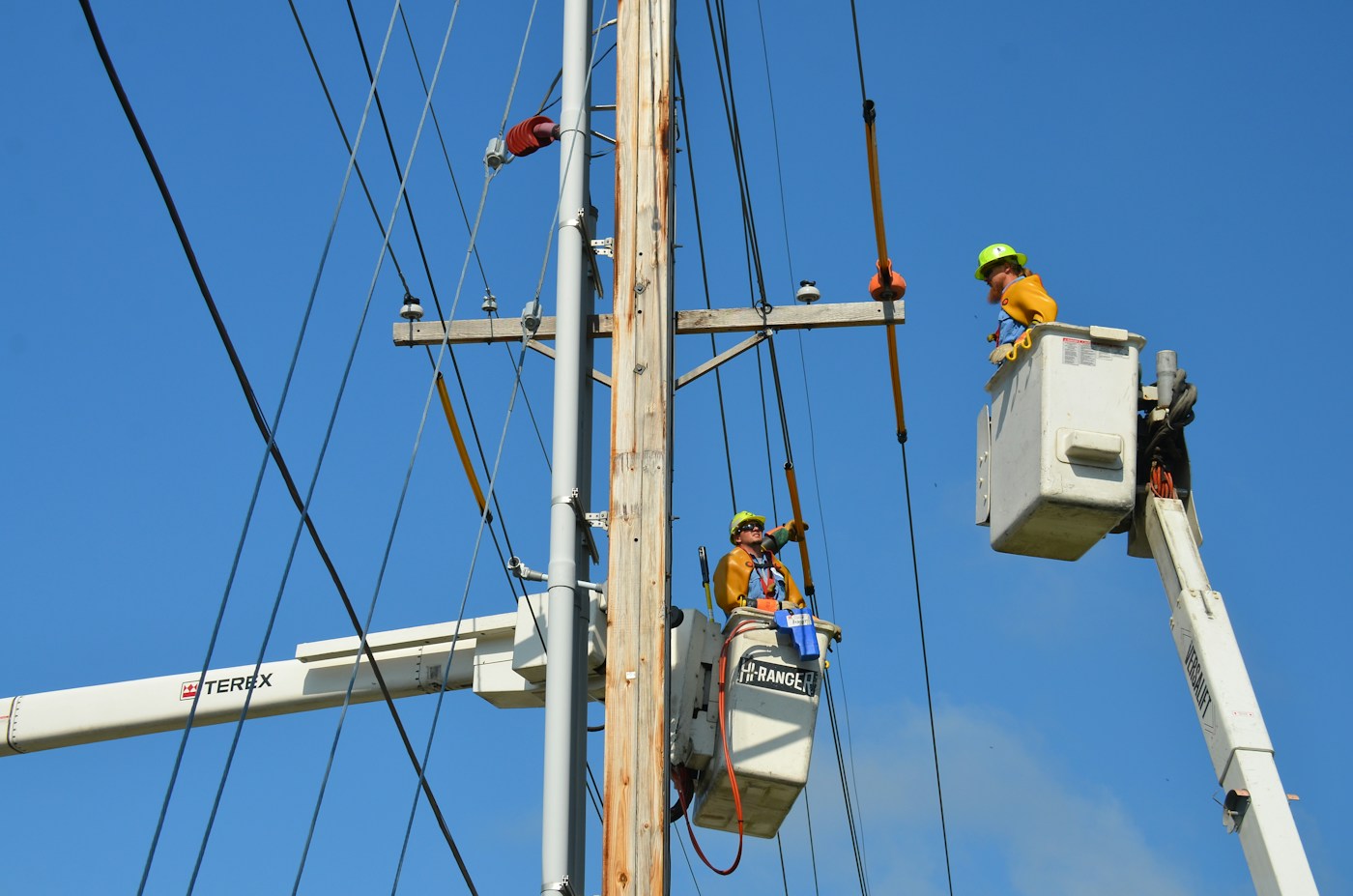 Two utility lineworkers working from elevated buckets beside a power pole